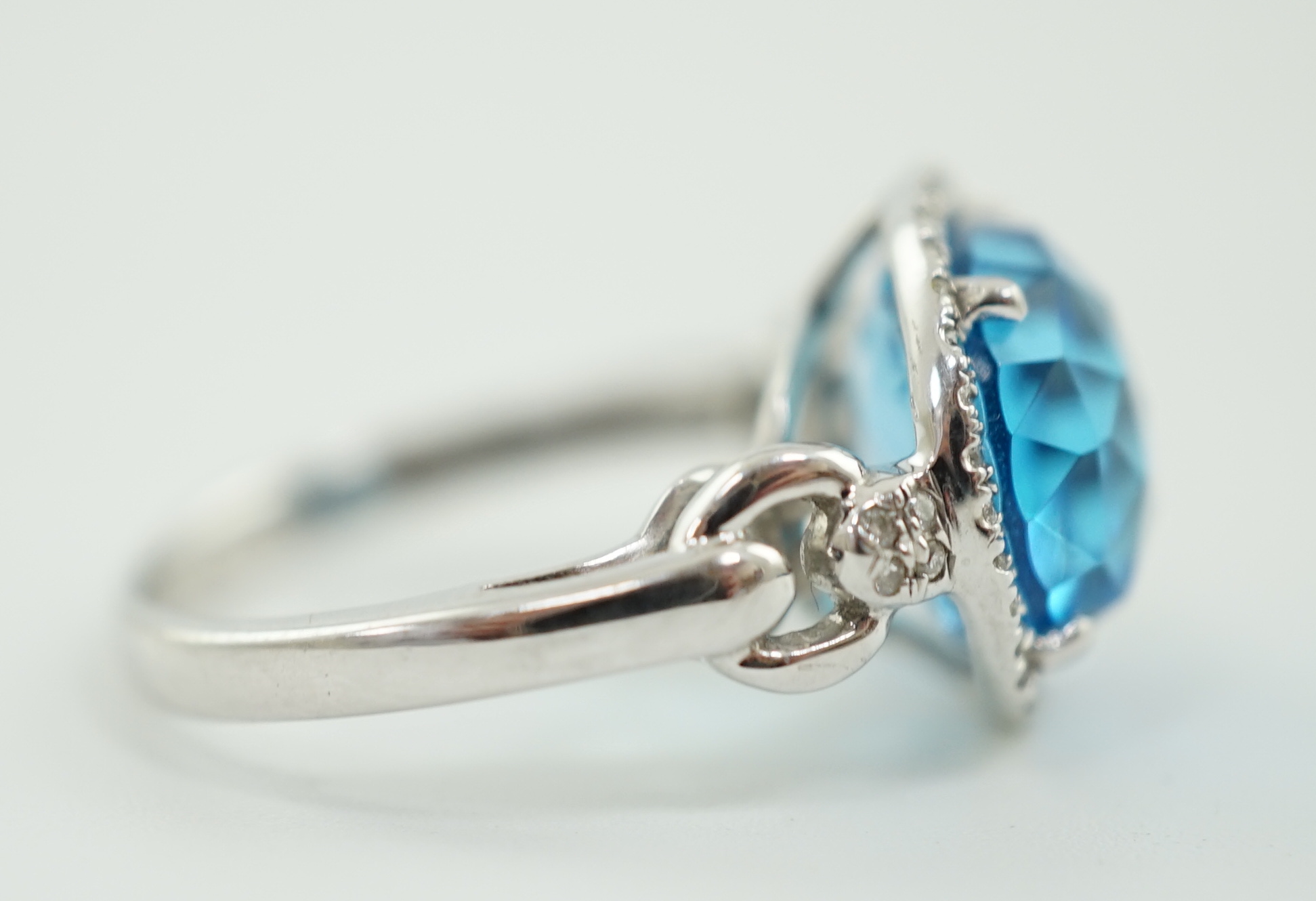 A modern 18ct white gold and facetted oval cut blue topaz set dress ring, with diamond chip set border and shoulders